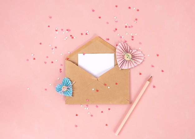 Corações de papel na técnica de scrapbooking e rosa e vermelho doces corações de açúcar doces voam fora do envelope de papel ofício sobre o fundo de coral vivo