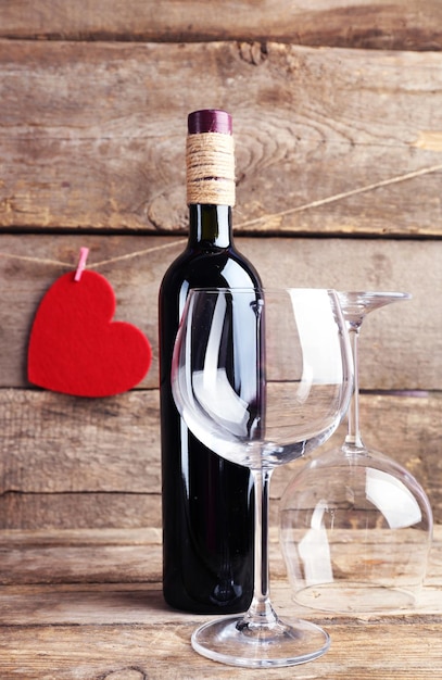 Corações vermelhos com garrafa de vinho e copos em fundo de madeira