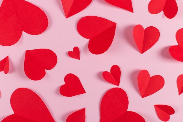 Corações vermelhos são feitos à mão em fundo rosa. Preparação para o dia dos namorados com um lugar para texto. Copie o espaço.