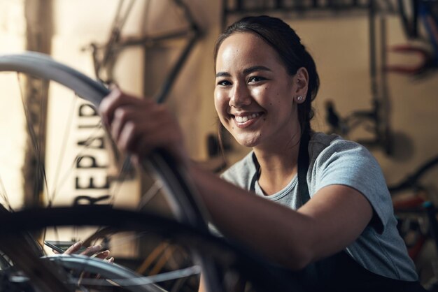 Un corazón agradecido una mente agradecida Retrato de una mujer joven que parece extremadamente complacida mientras sostiene un teléfono celular y arregla una bicicleta en un taller de reparación de bicicletas