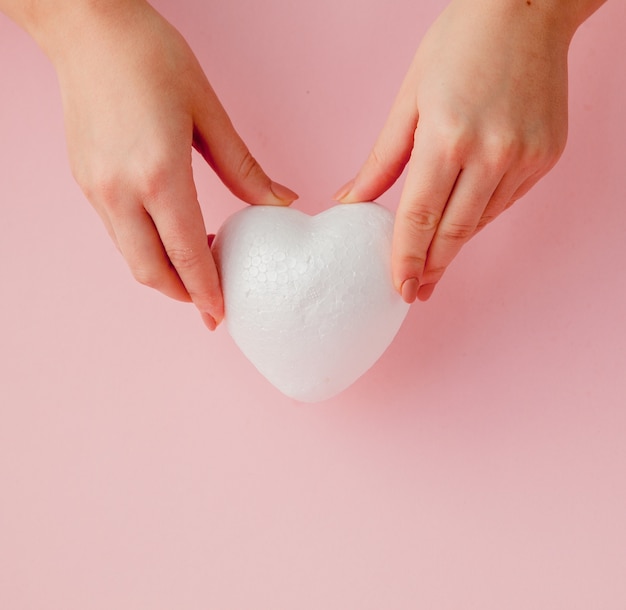 Corazón de amor blanco vacío en manos en mesa rosa