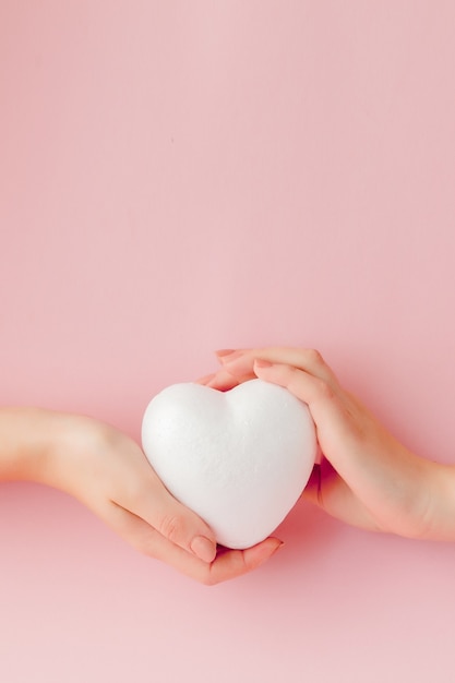 Corazón de amor vacío blanco en manos sobre fondo rosa.