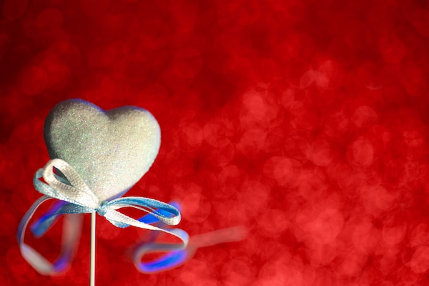 Un corazón con un arco. Bokeh borrosa rojo en el fondo. El concepto para el día de San Valentín