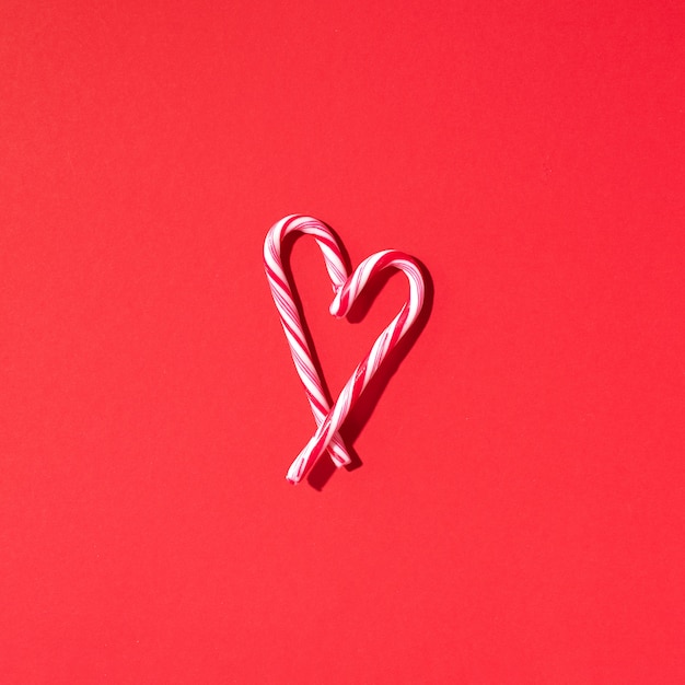 Corazón de bastón de caramelo de Navidad sobre fondo rojo con espacio de copia. Vista superior. Amor, concepto de día de San Valentín. Año nuevo y tarjeta de navidad