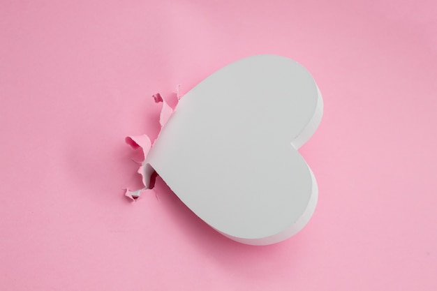 Corazón blanco haciendo un agujero en el fondo de papel rosa