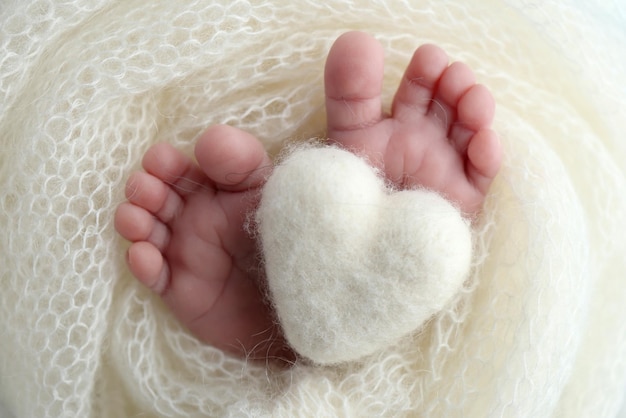 Corazón blanco de punto en las piernas de un bebé Fotografía macro El diminuto pie de un bebé recién nacido Pies suaves de un recién nacido en una manta de lana blanca Primer plano de los talones de los dedos de los pies y los pies de un recién nacido