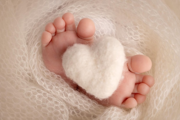 Corazón blanco de punto en las piernas de un bebé Pies suaves de un recién nacido en una manta de lana blanca Primer plano de los talones de los pies y los pies de un recién nacido Fotografía macro del pie diminuto de un bebé recién nacido