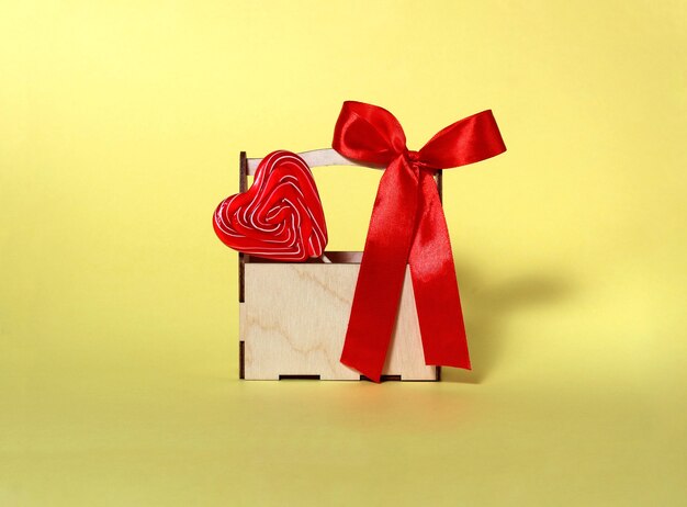 Corazón de caramelo en caja de madera con lazo rojo sobre superficie amarilla