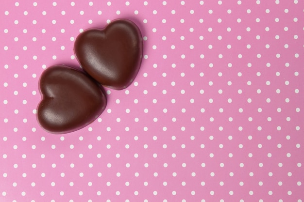 Corazón de caramelo de chocolate dos sobre fondo rosa con lunares, día de San Valentín, de cerca con espacio de copia