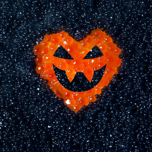 Corazón de caviar rojo con cara de Halloween sobre un fondo de caviar negro