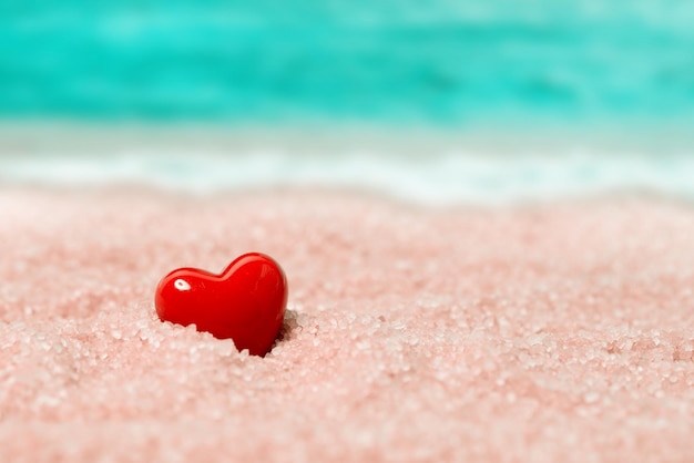 Corazón de cerámica roja en la arena en el fondo de la playa y el mar