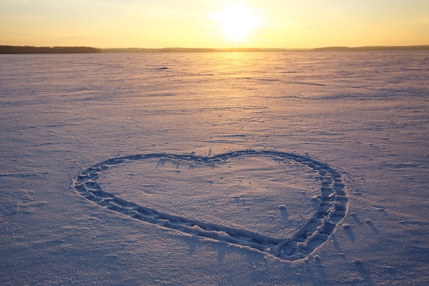 Un corazón se dibuja en la nieve. Puesta de sol de fondo.