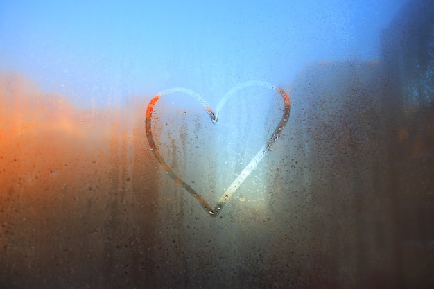 Un corazón dibujado con un dedo en una ventana empañada contra la ciudad