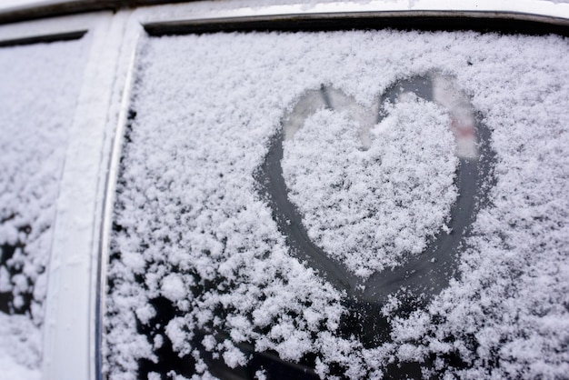 Corazón dibujado en el parabrisas de un coche cubierto de nieve fresca de Navidad