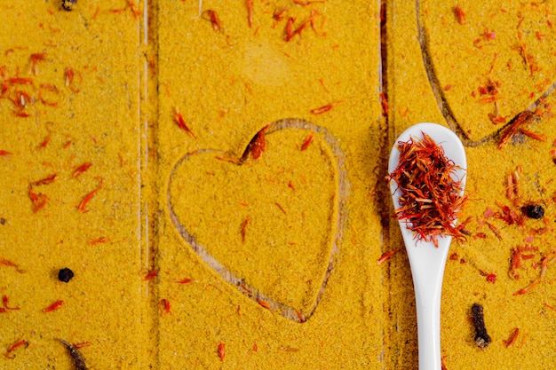 Foto corazón de especias y condimentos. cuchara blanca con azafrán al curry