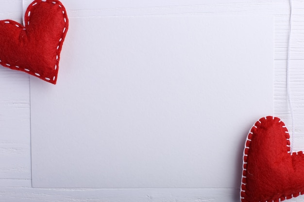 Corazón de fieltro rojo hecho a mano junto a papel blanco sobre mesa de madera