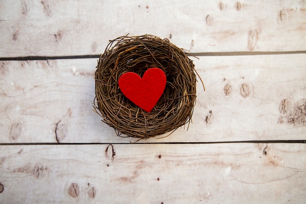Corazón de fieltro rojo na nido sobre fondo de madera