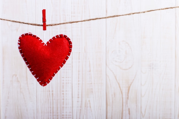 Corazón de fieltro rojo sobre una cuerda, sobre fondo blanco de madera