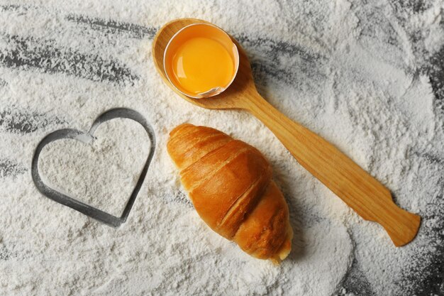 Corazón de harina, croissant y cuchara de madera sobre fondo gris