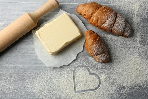 Corazón de harina, croissant y utensilios de cocina de madera sobre fondo gris