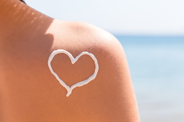 El corazón hecho de crema solar se dibuja en el hombro de la mujer en la playa.