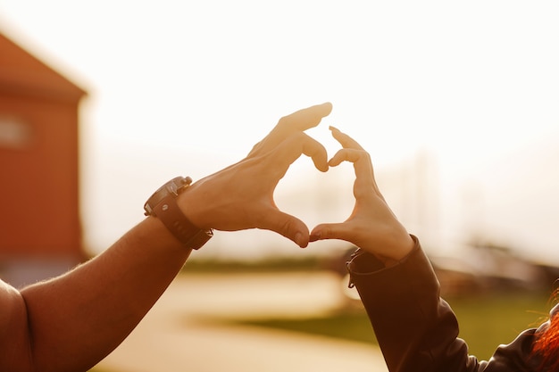 Corazón hecho de las manos de un chico y una chica al atardecer.