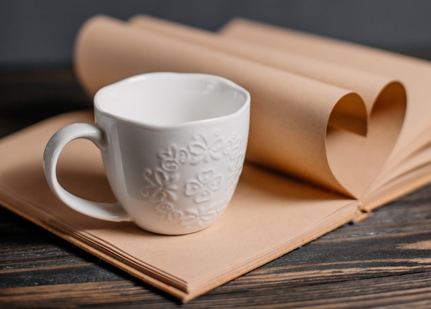 Corazón de hojas de libros con una taza de luces, amor y concepto de San Valentín en una mesa de madera