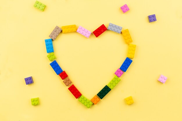 Foto corazón de juguete bloques de construcción de plástico de colores sobre fondo amarillo