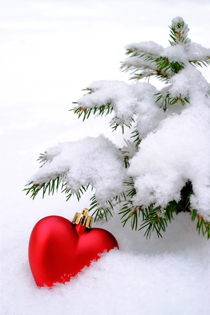 Foto corazón de juguete rojo en el árbol de navidad en la nieve.