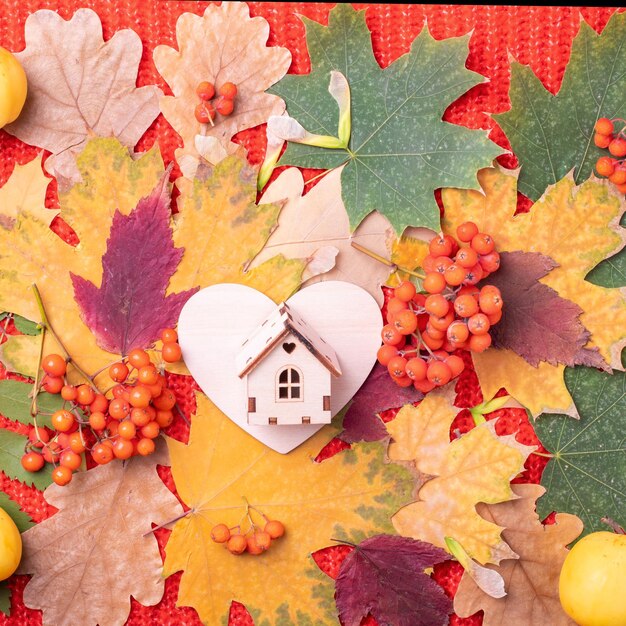 Corazón de madera y casa de madera de juguete en hojas de otoño caídas secas de color rojo naranja verde Concepto de amor de otoño Concepto de apoyo en otoño Concepto de familia