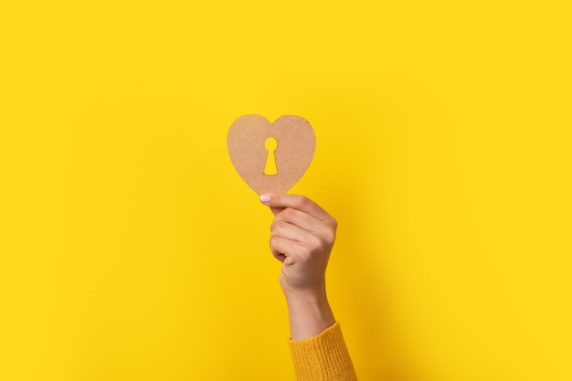 Corazón de madera con ojo de cerradura en mano sobre fondo amarillo
