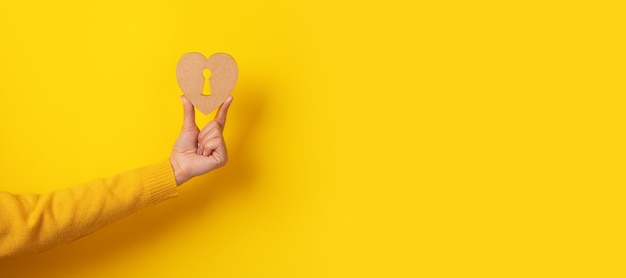 Foto corazón de madera con ojo de cerradura en la mano sobre fondo amarillo