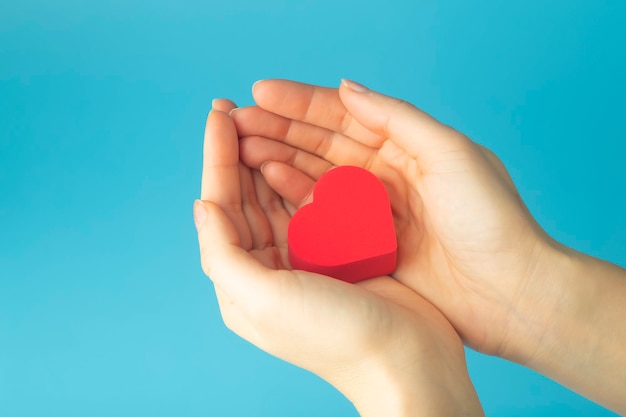 Corazón en manos de una mujer sobre un fondo de color. Fondo para San Valentín (14 de febrero) y amor.