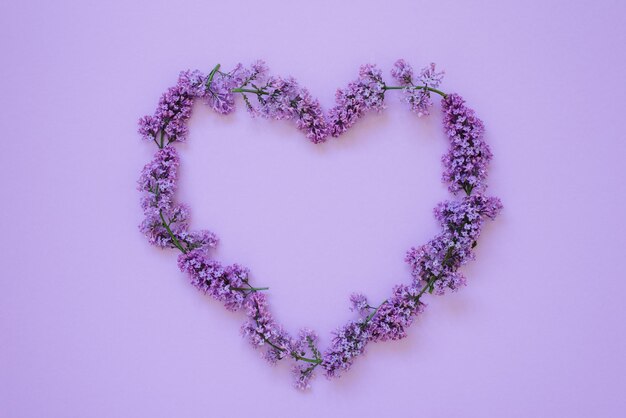 Corazón de marco de ramas lilas sobre fondo violeta Vista superior endecha plana