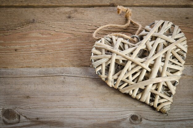 Corazón de mimbre hecho a mano acostado del lado derecho sobre una base de madera. Vista superior