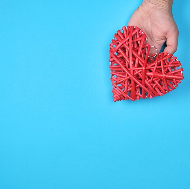 Corazón de mimbre rojo de madera en una mano femenina en un azul