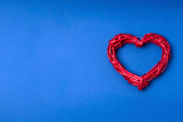 Foto corazón de mimbre rojo sobre fondo azul.