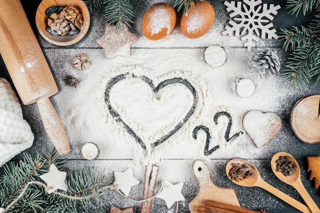 Corazón y números 22 en harina con ramas de árbol de Navidad, accesorios e ingredientes para hornear. Feliz año nuevo 2022