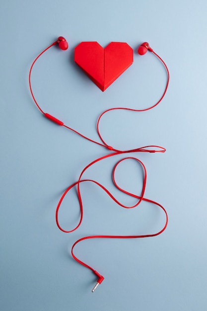 Corazón de origami rojo con auriculares en mesa azul