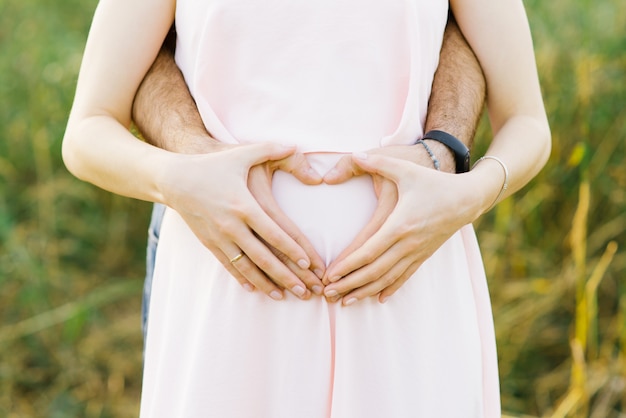 Corazón de las palmas del esposo y la esposa en el vientre de una mujer embarazada