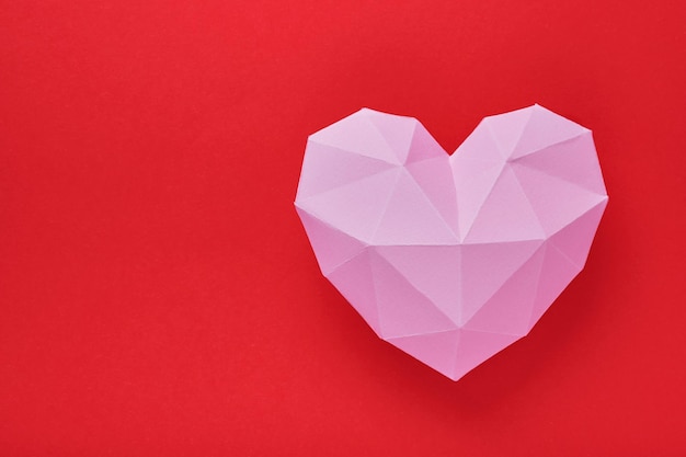 Corazón de papel rosa aislado sobre fondo rojo. Corazón de papel poligonal rojo para el día de San Valentín o cualquier otra tarjeta de invitación de amor. Vista superior, espacio de copia.