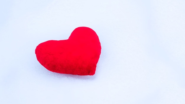 Corazón de peluche rojo sobre la nieve.