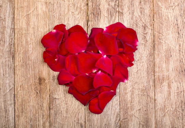 Corazón de pétalos rojos sobre mesa de madera