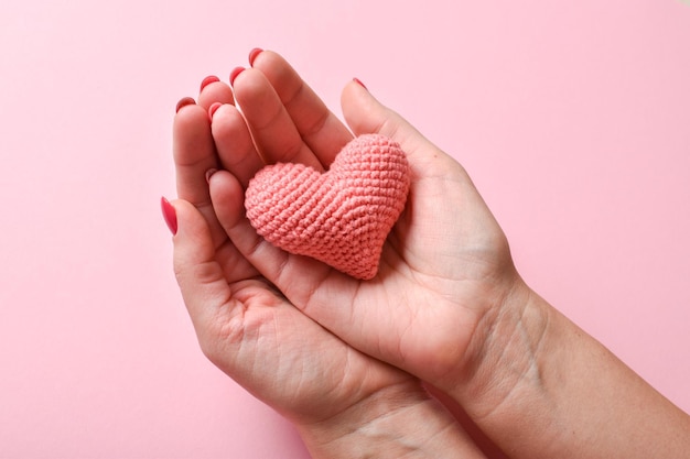 Corazón de punto rosa en manos de una chica con una hermosa manicura en un fondo rosa Amor