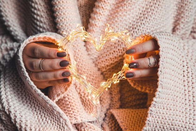 Corazón resplandeciente en manos de una mujer. Feliz día de San Valentín. Cuadros, comodidad, invierno, corazón de alas de guirnalda en manos de una mujer. Feliz día de San Valentín