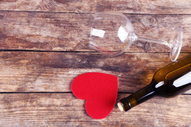 Corazón rojo con botella de vino y copas sobre fondo de madera