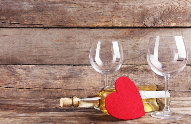 Corazón rojo con botella de vino y copas sobre fondo de madera