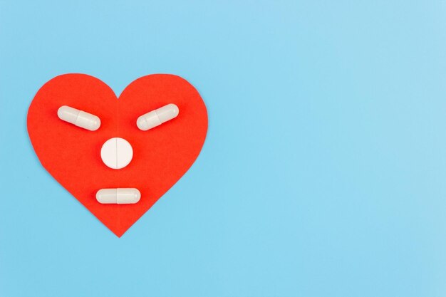 Corazón rojo con una cara hecha de pastillas sobre un fondo azul. El concepto de medicamentos, suplementos dietéticos, vitaminas para el tratamiento del corazón y la prevención de enfermedades. Copie el espacio.