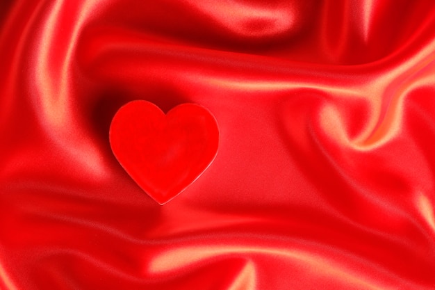 El corazón rojo se encuentra contra el romance de tela de seda roja de fondo