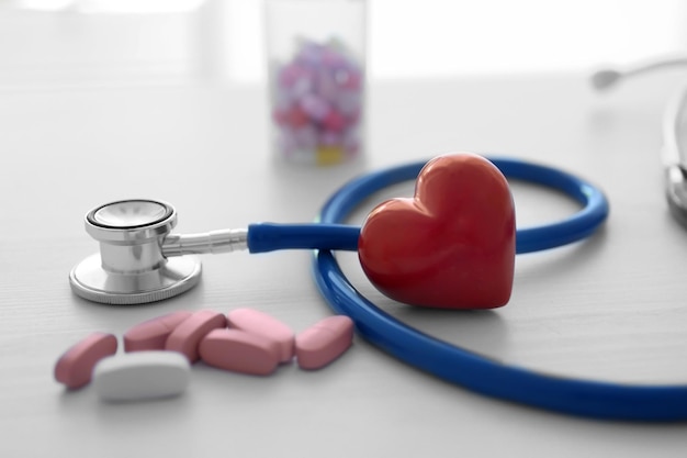 Corazón rojo con estetoscopio y pastillas en la mesa